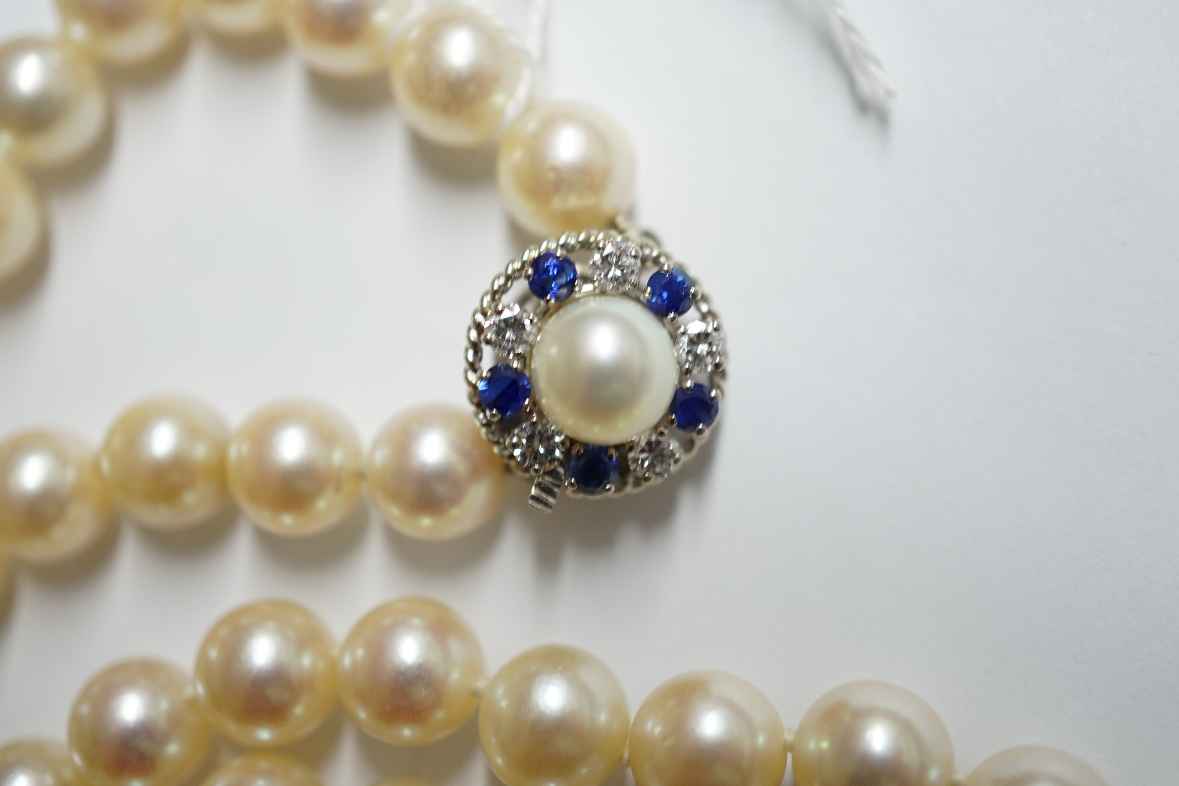 A single strand cultured pearl necklace, with French white metal (18ct mark), sapphire, diamond and cultured pearl set clasp, bearing the signature 'Cartier', 60cm. Condition - fair